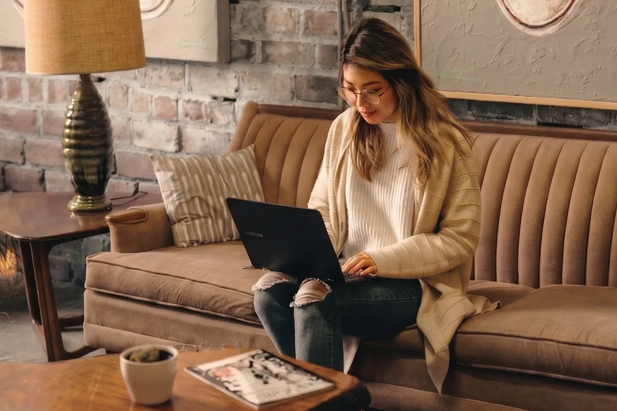 A person working on a laptop on a sofa in a warm, brick-walled lounge