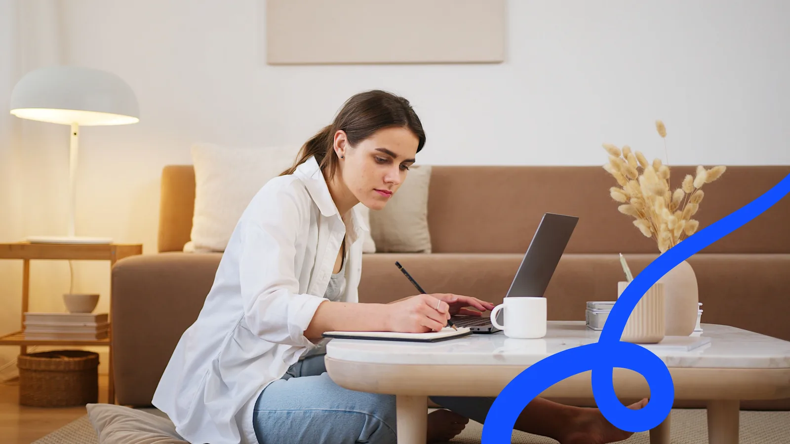 Someone taking notes beside a laptop while pulling a report together